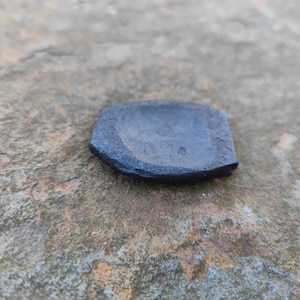 Op de afbeelding: Een klein, zwart, keramisch schaaltje met een licht afgeronde vorm en een ruw, getextureerd oppervlak.