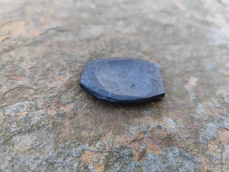 Op de afbeelding: Een klein, zwart, keramisch schaaltje met een licht afgeronde vorm en een ruw, getextureerd oppervlak.