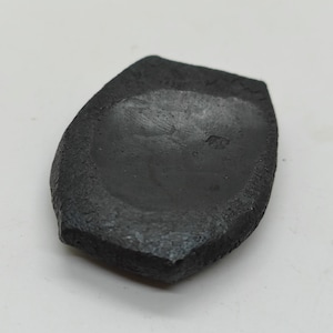 Op de afbeelding: Een zwarte, onregelmatig gevormde, keramische schaal met een licht concave bodem. De schaal heeft een ruw, getextureerd oppervlak.