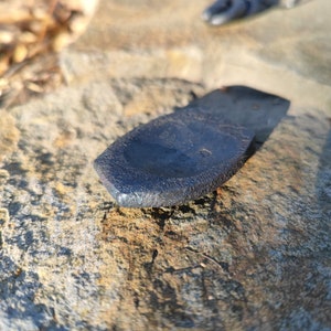 Op de afbeelding: Een donkergrijs metalen wigvormig object dat op een ruw, lichtbruin en grijs rotsoppervlak ligt.
