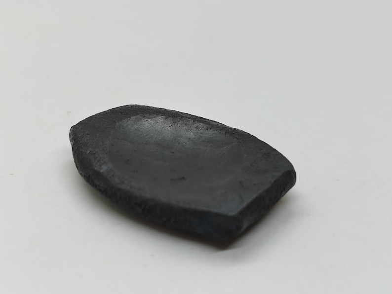 Op de afbeelding: Een klein, zwart, keramisch schaaltje met een licht afgeronde, ovale vorm. Het schaaltje heeft een ruw, getextureerd oppervlak en een licht ingedeukt midden.