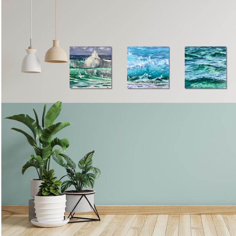 May include: Three framed paintings of ocean waves. The paintings are in shades of blue and green, with white foam crests. The paintings are hung on a white wall with a light blue accent wall below.