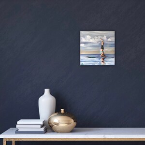 May include: A painting of a person doing a handstand on a paddleboard in the water. The sky is blue with white clouds. The water is a light blue color.