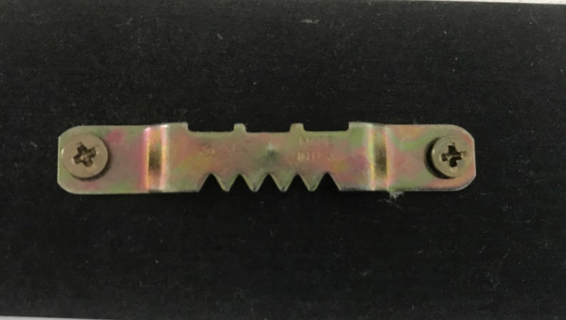 May include: A metal picture hanging hook with two screws. The hook has a serrated edge and the text "MADE IN U.S.A." is visible.