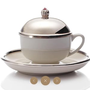 May include: A white porcelain teacup and saucer with a silver lid. The lid has a small red jewel on top.