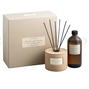 May include: A brown cardboard box with a white label that reads "Atelier Rebul My Beautiful Garden White Tea Leaves & Fresh Herbs Reed Diffuser". The box is next to a brown diffuser with black reeds and a clear glass bottle of diffuser oil with a brown label that reads "Atelier Rebul My Beautiful Garden".
