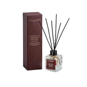 May include: A clear glass reed diffuser with black reeds and a dark brown box. The box and the diffuser label read "ATELIER REBUL" and "CIRAGAN PALACE". The diffuser has a gold chain and a red tassel.