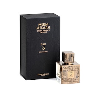 May include: A black box with gold lettering that reads "Parfum Artisanal Grande Pharmacie Parisienne Elixir 3 Extrait Parfum Atelier Rebul". The box is next to a glass bottle of perfume with a gold cap and label that reads "Atelier Rebul Elixir 3 Parfum Artisanal Grande Pharmacie Parisienne".