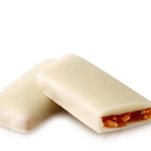 Op de afbeelding: Twee rechthoekige witte chocoladerepen met een vulling van karamel en noten. Eén reep is heel, de andere is doorgesneden om de vulling te laten zien. Op een witte achtergrond.