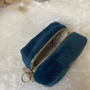 K&ouml;nnte beinhalten: Ein rechteckiges, tiefblaues, pl&uuml;schiges Etui mit Rei&szlig;verschluss, goldfarbenem Rei&szlig;verschluss und einer kleinen, glitzernden Schleife. Das Etui ist ge&ouml;ffnet und zeigt ein helles Innenfutter und einen goldfarbenen Ring am Rei&szlig;verschluss.