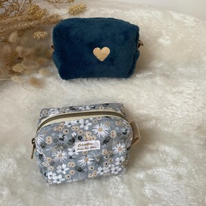 K&ouml;nnte beinhalten: Zwei kleine Kosmetiktaschen. Die obere Tasche ist aus tiefblauem Pl&uuml;sch mit einem Holzherz-Akzent. Die untere Tasche ist grau mit einem Blumenmuster, einem Rei&szlig;verschluss und einem kleinen Etikett "Colchiques dans les pr&eacute;s."