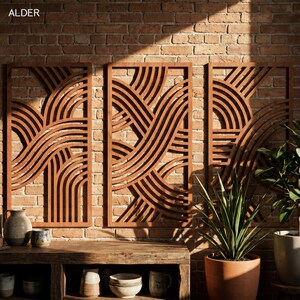 May include: Three wooden wall panels with a repeating wave-like design are mounted on a brick wall. The panels are a warm brown color and have a rectangular shape. The word "ALDER" is in the top left corner.