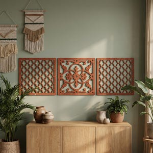 May include: Three wooden wall panels with intricate cut-out designs. The center panel features a floral pattern, while the flanking panels have a repeating geometric design. The panels are a warm brown color and are mounted on a light green wall. Decorative home decor.