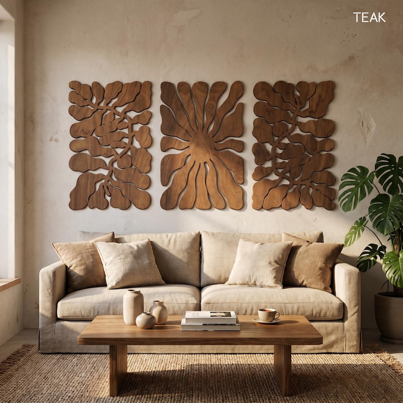 K&ouml;nnte beinhalten: Drei Wandpaneele aus Teakholz mit organischen, bl&uuml;tenartigen Designs. Die Paneele sind &uuml;ber einem beigen Sofa mit passenden Kissen angebracht. Ein Couchtisch aus Holz und eine Topfpflanze vervollst&auml;ndigen die Wohnzimmereinrichtung.