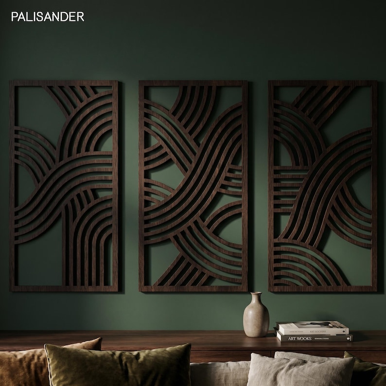 May include: Three dark brown wooden wall panels with a wave-like design against a dark green wall. The panels are rectangular with a repeating pattern of curved lines. A small vase and books are on a wooden surface below.