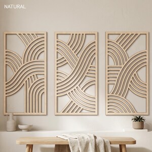 May include: Three rectangular wooden wall art panels with a natural finish. Each panel features a layered, abstract design of curved lines and arches. The word "NATURAL" is printed in the top left corner. The panels are displayed above a wooden bench.