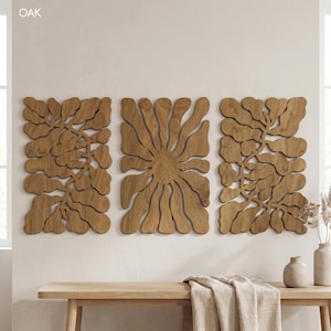 K&ouml;nnte beinhalten: Drei Wandpaneele aus Holz mit nat&uuml;rlicher Holzoberfl&auml;che. Die Paneele zeigen ein abstraktes Blumendesign, mit dem Wort "OAK" in der oberen linken Ecke. Die Paneele sind &uuml;ber einer Holzbank mit dekorativen Vasen und einem gefalteten Tuch angebracht.
