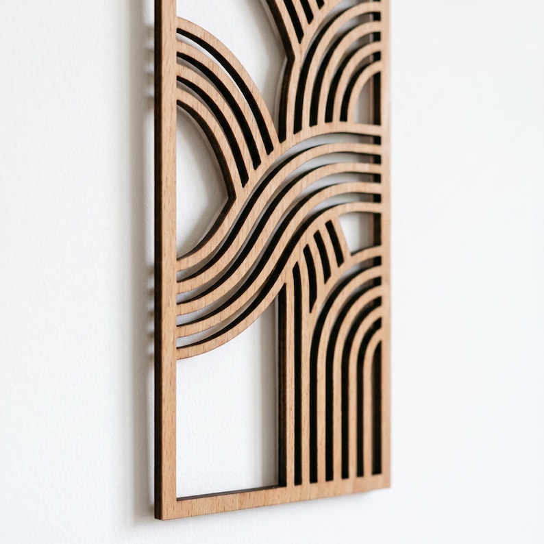 May include: A wooden wall art piece with a geometric design. The art features layered, curved lines and arches, creating a wave-like pattern. The wood has a natural, light brown color, and the piece is framed.