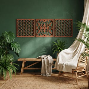 May include: Three decorative wooden wall panels with intricate geometric and floral cut-out designs. The panels are a warm reddish-brown color and are mounted on a dark green wall. The room also features a wooden bench, plants, and a woven rug.