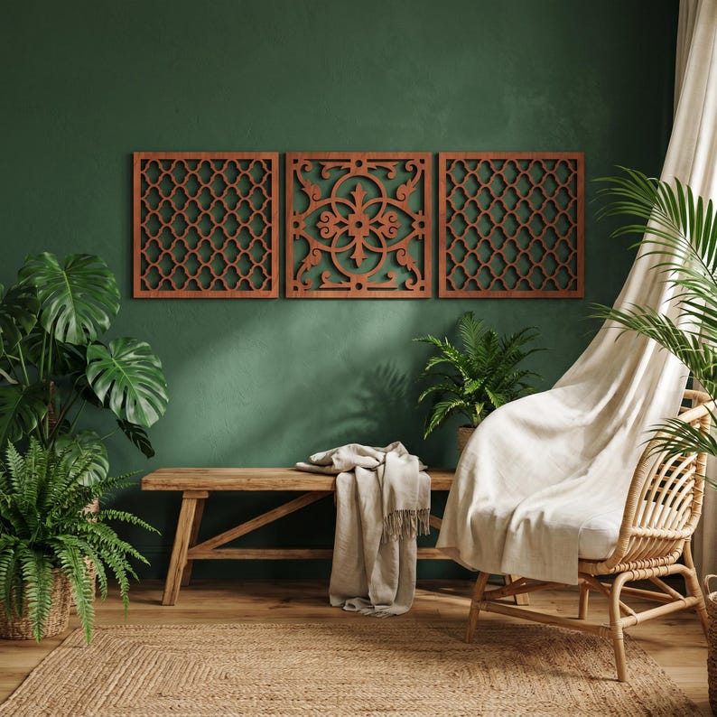 May include: Three decorative wooden wall panels with intricate geometric and floral cut-out designs. The panels are a warm reddish-brown color and are mounted on a dark green wall. The room also features a wooden bench, plants, and a woven rug.