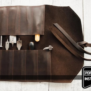 以下が含まれることがあります： フラップ留めとストラップが付いた茶色の革製のツールロール。ロールが開いており、ドリルビット、ドライバー、ノミなど、さまざまなツールが入っています。黒いタグに「PDF PATTERN + INSTRUCTION」というテキストが表示されています。