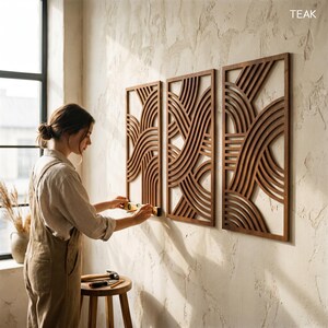 May include: Three rectangular wooden wall panels with a repeating wave design are mounted on a textured wall. The panels are a warm brown color. A person is shown installing the panels with tools.