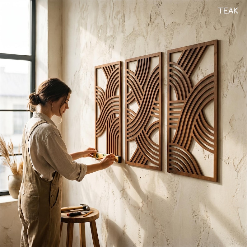 May include: Three rectangular wooden wall panels with a repeating wave design are mounted on a textured wall. The panels are a warm brown color. A person is shown installing the panels with tools.