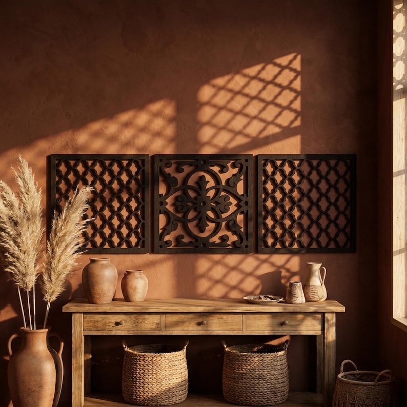 May include: Three dark brown decorative wall panels with intricate geometric and floral patterns. The panels are mounted on a terracotta-colored wall above a wooden console table. The table features two woven baskets, vases, and dried pampas grass.