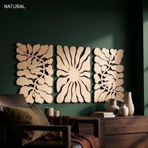 K&ouml;nnte beinhalten: Drei Wandpaneele aus Holz mit nat&uuml;rlicher Oberfl&auml;che, jedes mit einem floralen oder blattartigen Design. Die Paneele sind an einer dunkelgr&uuml;nen Wand angebracht. Das Wort "NATURAL" befindet sich in der oberen linken Ecke.