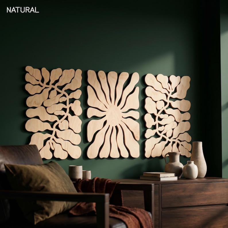 K&ouml;nnte beinhalten: Drei Wandpaneele aus Holz mit nat&uuml;rlicher Oberfl&auml;che, jedes mit einem floralen oder blattartigen Design. Die Paneele sind an einer dunkelgr&uuml;nen Wand angebracht. Das Wort "NATURAL" befindet sich in der oberen linken Ecke.