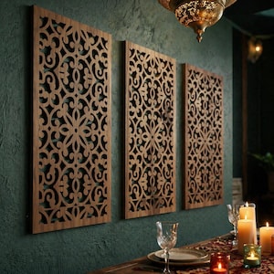 Könnte beinhalten: Drei rechteckige Holz-Wandpaneele mit aufwendigen, durchbrochenen floralen und scrollartigen Designs. Die Paneele sind warmbraun und an einer dunkel türkisfarbenen Wand befestigt. Die Paneele sind Teil einer Wohnkultur-Kollektion.
