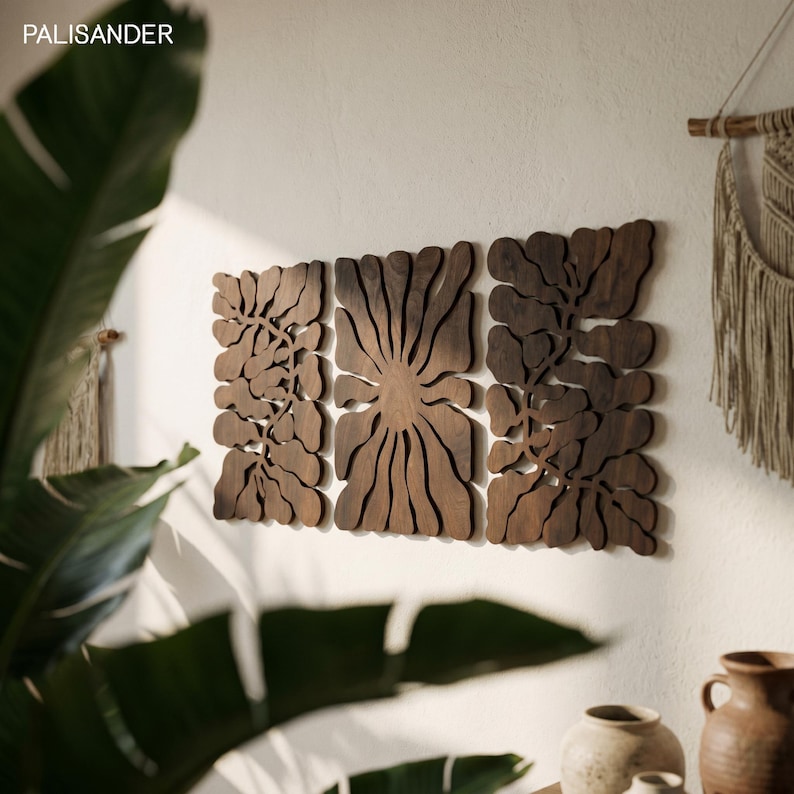 K&ouml;nnte beinhalten: Drei dunkelbraune Wandkunstpaneele aus Holz mit floralem Design sind an einer wei&szlig;en Wand befestigt. Die Paneele sind mit komplizierten Mustern geschnitten. Das Wort "PALISANDER" befindet sich in der oberen linken Ecke.