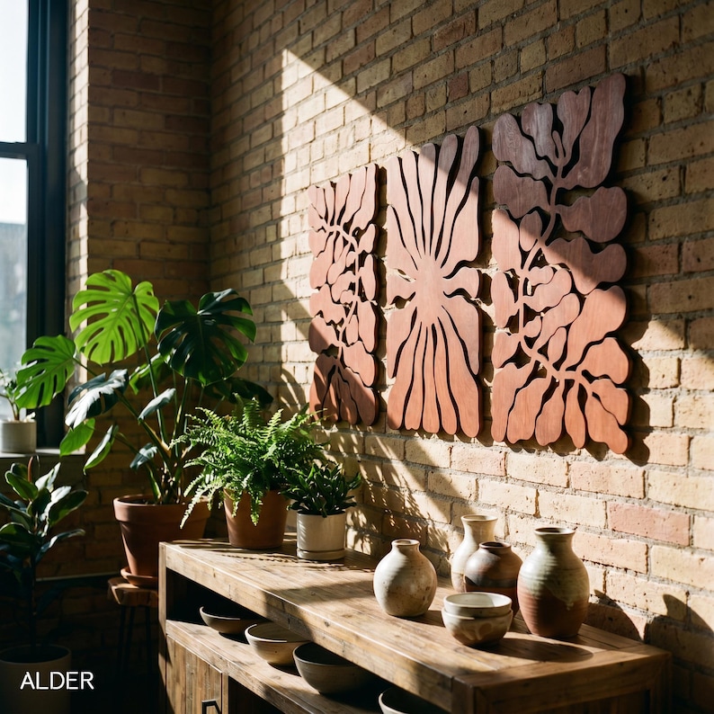 K&ouml;nnte beinhalten: Holzwandkunst mit floralem Design, an einer Backsteinmauer befestigt. Die Kunst hat einen warmen, r&ouml;tlich-braunen Farbton. Ein Holztisch zeigt verschiedene Keramikvasen und Schalen. Topfpflanzen sorgen f&uuml;r einen Hauch von Gr&uuml;n.