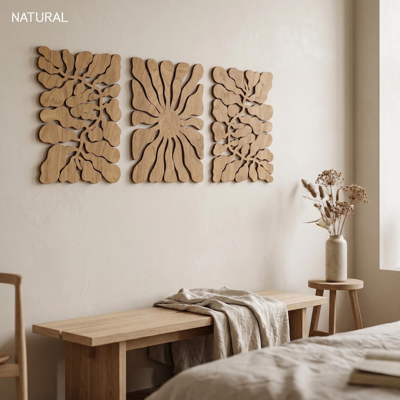K&ouml;nnte beinhalten: Drei Wandkunstpaneele aus Holz mit floralem Design sind an einer hellen Wand angebracht. Unter der Kunst befindet sich eine Holzbank mit einer gefalteten Decke. Das Wort "NATURAL" befindet sich in der oberen linken Ecke.
