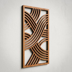May include: A rectangular wooden wall art piece with a geometric design. The art features a series of curved, parallel lines that intersect and overlap, creating a woven or wave-like pattern. The wood has a warm, natural tone.