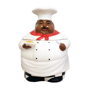 Op de afbeelding: Een keramische koekjespot in de vorm van een chef-kok. De chef-kok draagt een wit uniform met een rode halsdoek en een hoge witte hoed. De basis van de pot heeft een zwart-wit geblokt patroon.