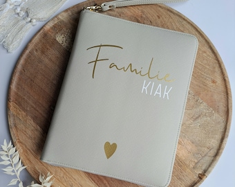 以下が含まれることがあります： 金色のハートと「Familie Klak」という金と白の文字が書かれた薄い灰色のジッパー付きポーチです。