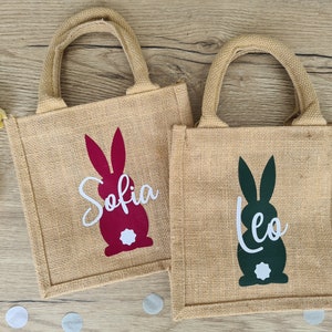 Op de afbeelding: Twee jute tassen voor paasgeschenken met konijnen silhouetten. De tas links heeft een rood konijn met de naam "Sofia" in wit. De tas rechts heeft een groen konijn met de naam "Leo" in wit.