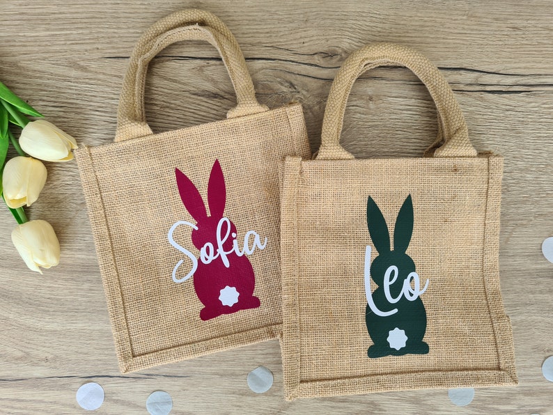 Op de afbeelding: Twee jute tassen voor paasgeschenken met konijnen silhouetten. De tas links heeft een rood konijn met de naam "Sofia" in wit. De tas rechts heeft een groen konijn met de naam "Leo" in wit.