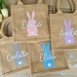 Op de afbeelding: Vier kleine jute tassen met konijnenontwerpen en gepersonaliseerde namen. De tassen zijn in roze, paars, grijs en blauw. De namen op de tassen zijn Emilia, Amelie, Carlotta en Elijah.
