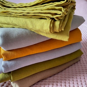 May include: A stack of seven linen fabric swatches in various shades of green, yellow, and beige. The swatches are folded and arranged in a pyramid shape.