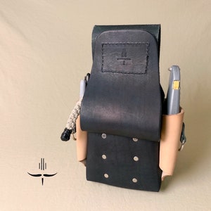 May include: Black leather tool belt with a tan leather side pouch and a silver metal buckle. The belt has a small black leather patch with a logo on it.