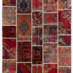 May include: A patchwork rug made from various vintage rugs, featuring a mix of red, blue, and beige colors with intricate floral and geometric patterns. The rug is stitched together with white thread and has a frayed edge.