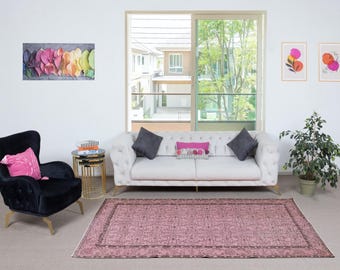 Könnte beinhalten: Wohnzimmer mit weißem Sofa, schwarzem Sessel und rosa Teppich. Der Raum ist mit Kunstwerken, Kissen und einem kleinen Beistelltisch mit Büchern dekoriert. Ein großes Fenster bietet einen Blick nach draußen.