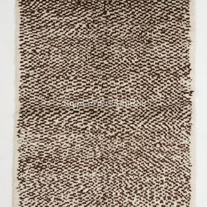 May include: A white and brown Moroccan rug with a textured, woven design. The rug has a fringe border.