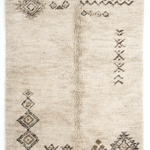 May include: A cream-coloured Moroccan rug with a geometric pattern in brown and black. The rug has a fringe border and is made of wool.