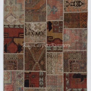 Puede incluir: Una alfombra de patchwork con una variedad de colores y patrones, incluyendo rojo, marrón, beige y azul. La alfombra está hecha de muchos cuadrados más pequeños que se han cosido juntos. La alfombra tiene un aspecto desgastado y descolorido, lo que le da un aspecto vintage.