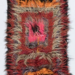 Peut inclure: Un tapis rectangulaire et hirsute avec un design géométrique vibrant. Le tapis présente des formes carrées et rectangulaires centrales dans des tons de rouge, d'orange, de noir et de rose. La texture du tapis est épaisse et duveteuse.