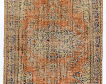 May include: A vintage rug with a faded orange background and intricate floral patterns in shades of blue, green, and beige. The rug has a border with a repeating floral design.