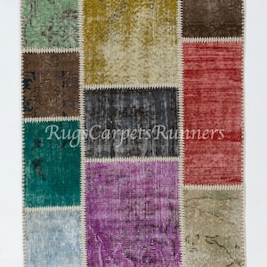 May include: A colorful patchwork rug with various shades of blue, green, purple, pink, and brown. The rug is made of different pieces of fabric sewn together, creating a unique and eclectic design.  "Rugs Carpets Runners" is printed on the rug.